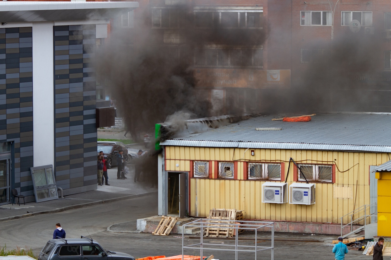 A single-floor yellow commercial building with smoke billowing out the sides from a fire.